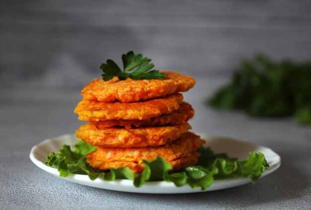 Natural dietary carrot pancakes on a plate with lettuce leaves and a fork on a gray background