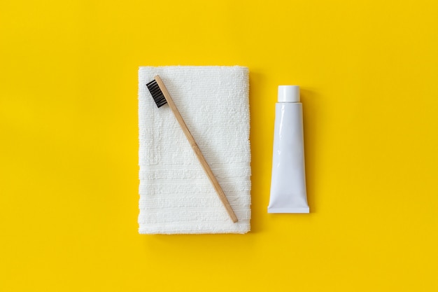 Natural eco-friendly bamboo brush on white towel and tube of toothpaste. 