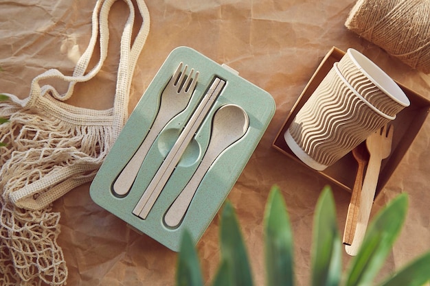 Natural ecological cutlery and cardboard cups with reusable bag on crumpled paper