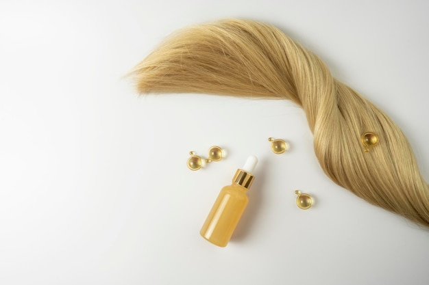 A natural essential oil or serum for hair care in golden capsules lying on a white table Hair care and smoothing concept