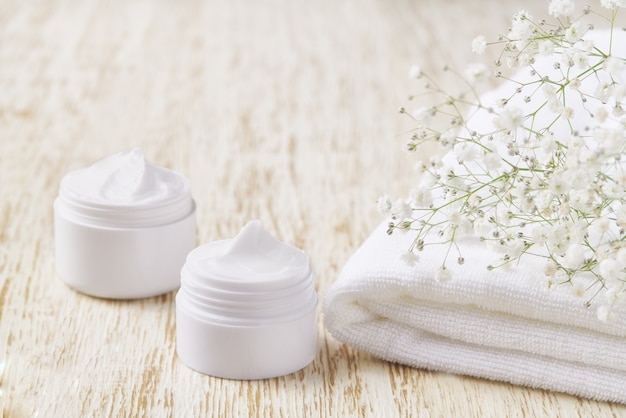 Natural face cream or lotion, organic cosmetic to moisturize the skin with towel and flowers in the background.