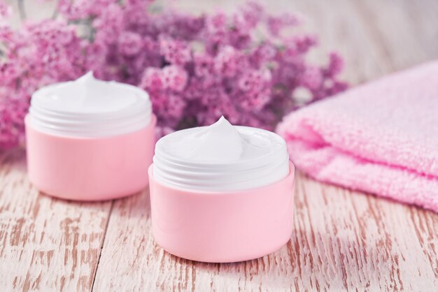 Natural face cream or lotion, organic cosmetic product to moisturize the skin with a towel and flowers on the background. Pink series  cosmetic.