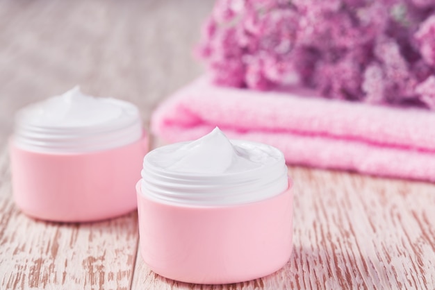 Natural face cream or lotion, organic cosmetic product to moisturize the skin with a towel and flowers on the background. Pink series  cosmetic.