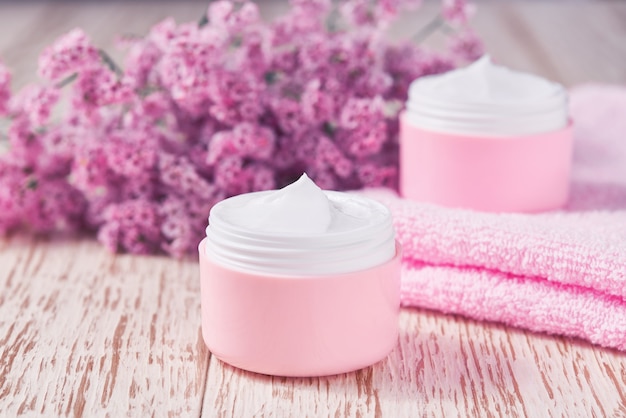 Natural face cream or lotion, organic cosmetic product to moisturize the skin with a towel and flowers on the background. Pink series  cosmetic.