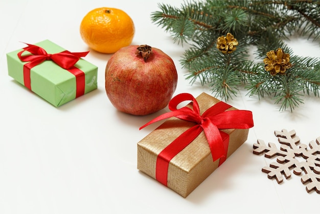 Natural fir tree branches with gift boxes and fruits on white background