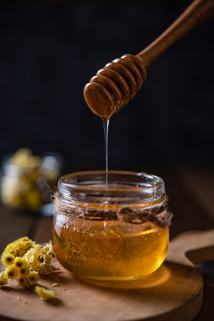 Natural floral honey drains to jar on wood background. Front view