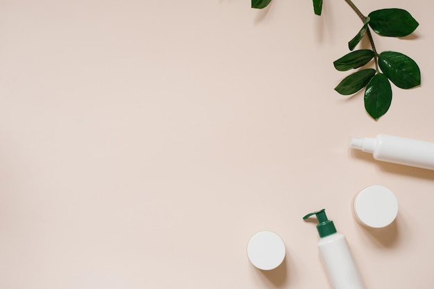 Natural herbal creams in bottles and jars with green leaves on a light beige background with copy space The concept of a natural organic cosmetic product Flat position top view