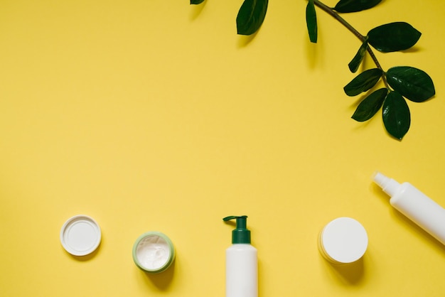 Natural herbal creams in bottles and jars with green leaves on a yellow background with copy space The concept of a natural organic cosmetic product Flat position top view