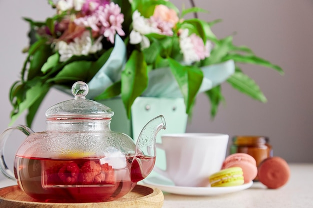 Natural herbal raspberry red tea in glass teapot macaroons and bouquet of flowers Aesthetic home breakfast Self care relaxing wellness lifestyle