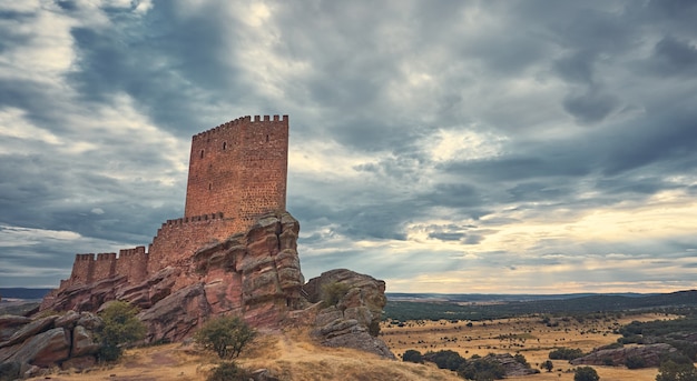 Natural landscape with a medieval castle on top of a hill and the suns rays through the clouds