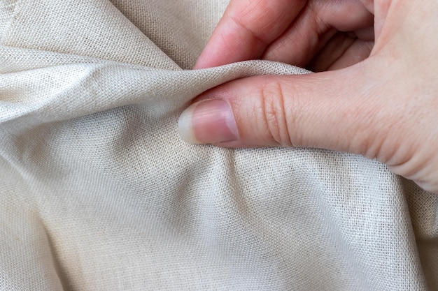 Natural linen fabric in woman hand rough crumpled burlap selective focus closeup view