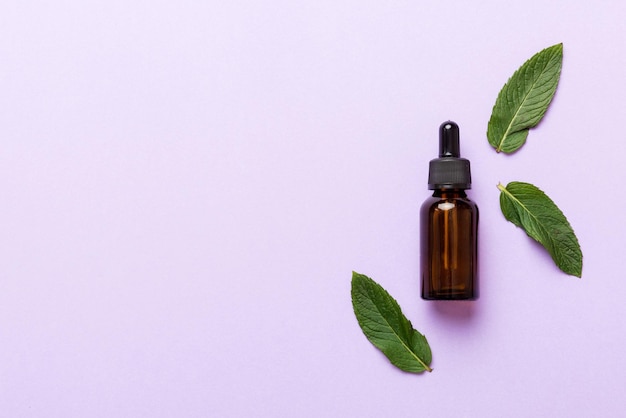 Natural Mint Essential Oil in a Glass Bottle organic cosmetics with herbal extracts of mint on colored background