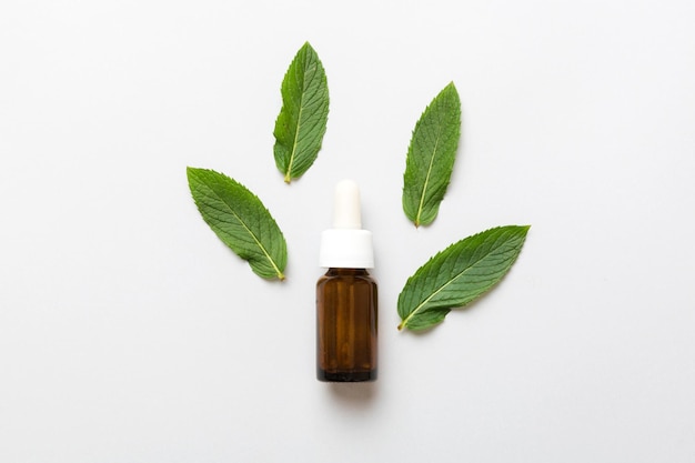 Natural Mint Essential Oil in a Glass Bottle organic cosmetics with herbal extracts of mint on colored background