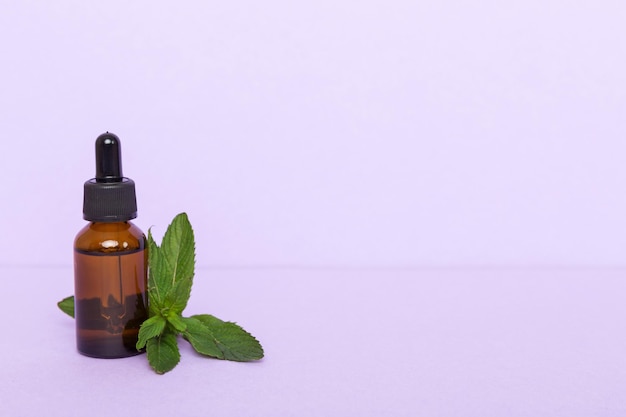 Natural Mint Essential Oil in a Glass Bottle organic cosmetics with herbal extracts of mint on colored background