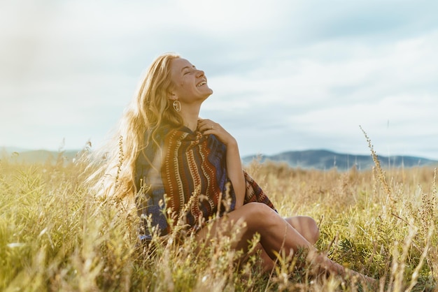 Natural natural beauty of the redhaired girl gleefully smiling sun and sky with an ethno cape on her