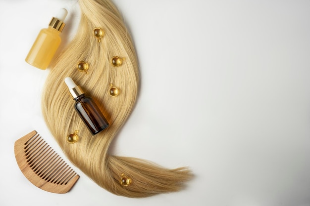 A natural oil or serum for hair care and a ply of blonde hair lying on a white background