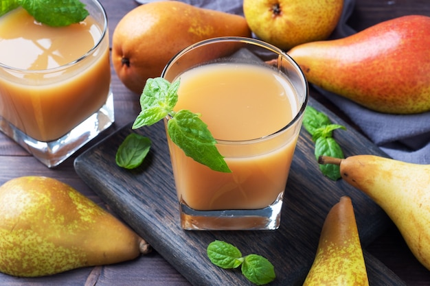 Natural pear juice in a glass cup. Juicy ripe conferences pears and mint leaves. Dark rustic wooden background.