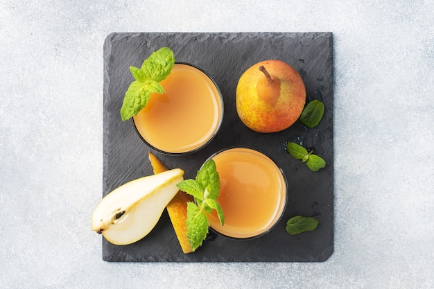 Natural pear juice in a glass cup. Juicy ripe conferences pears and mint leaves. top view Slate stand, light concrete background.