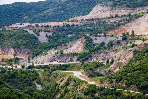 Natural quarry is located near road against backdrop of Rhodope Mountains and hills with forests and mountain vegetation