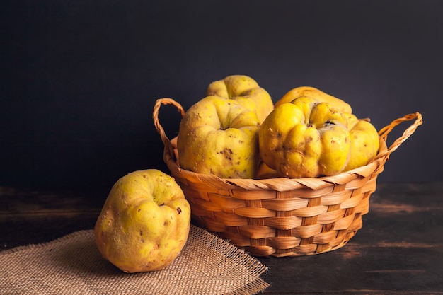 Natural quince fruit with defects in a basket on a jute napkin and a dark wooden background.