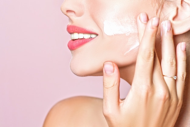 Natural skin. Close up beauty portrait of a laughing beautiful woman applying face cream. Clean and beauty facial concept.