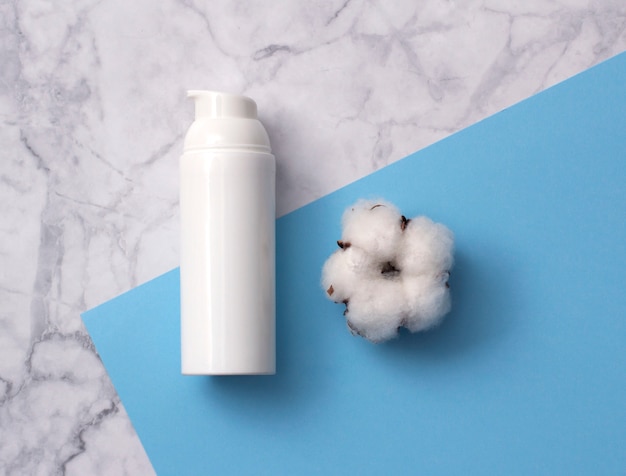 Natural skincare cosmetic product with cotton flower on white marble table from above.