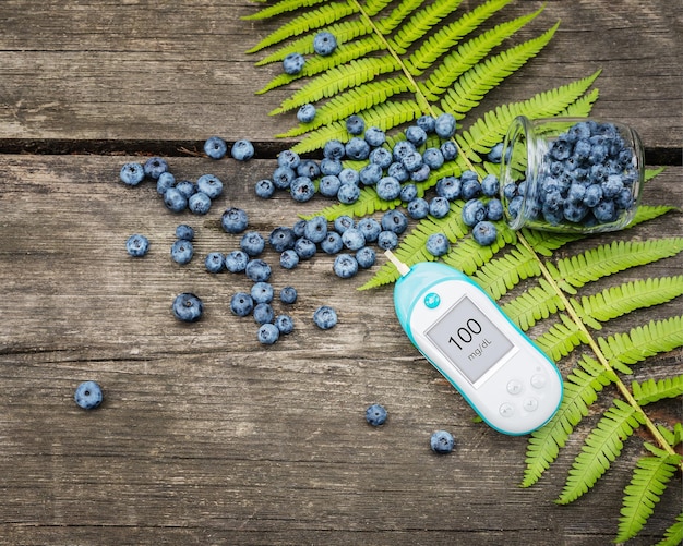 Natural wild blueberries blood glucose meter and fern leave on a wooden table