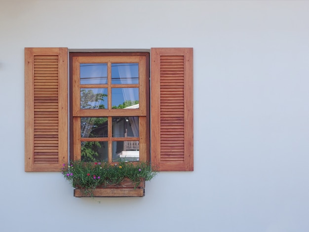 Natural wood windowwith hanging flower decor on cement wall.