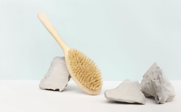 Natural wooden body brush balancing on rocks, on light-blue background. Massage, relax, spa.