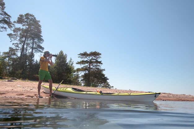 Naturalist photographer at work on the shore in a picturesque location Next to him is a kayak