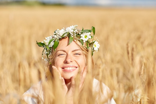 nature, summer holidays, vacation and people concept - face of happy smiling woman or teenage girl n in wreath of flowers on cereal field