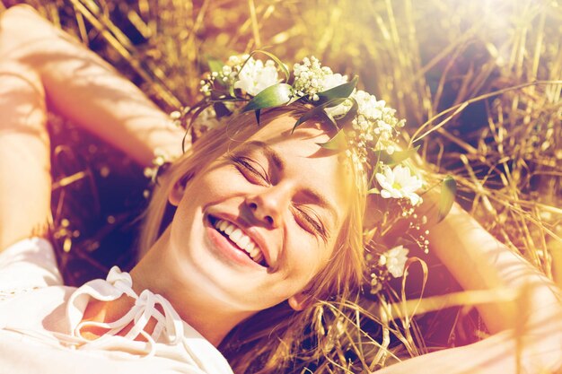 Photo nature, summer holidays, vacation and people concept - happy smiling woman in wreath of flowers lying on straw