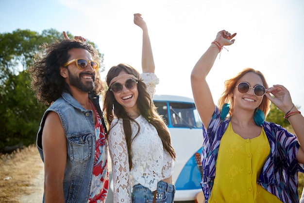 nature, summer, youth culture and people concept - happy young hippie friends dancing over minivan car outdoors