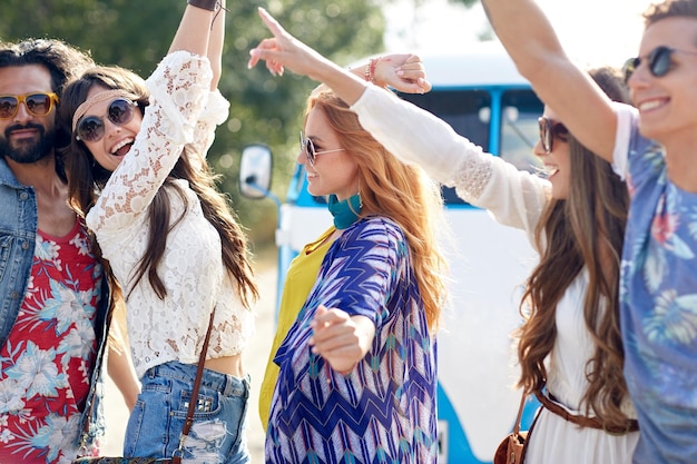 nature, summer, youth culture and people concept - happy young hippie friends dancing over minivan car outdoors