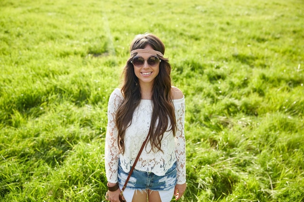 Photo nature, summer, youth culture and people concept - smiling young hippie woman in sunglasses on green field