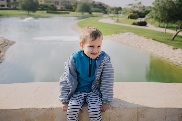 Naughty frolic playful walking preschool baby boy sit at bridge near lake