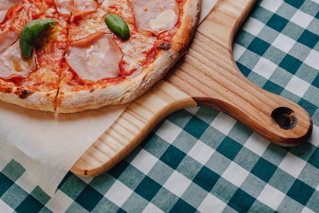 Neapolitan pizza with ham, cheese, arugula, basil, tomatoes sprinkled with cheese on a wooden board 