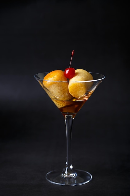 Neapolitan Rum baba or baba au rum in a martini glass with a cocktail cherry on a black background Small yeast cakes soaked in rum syrup Traditional Italian pastry Closeup selective focus