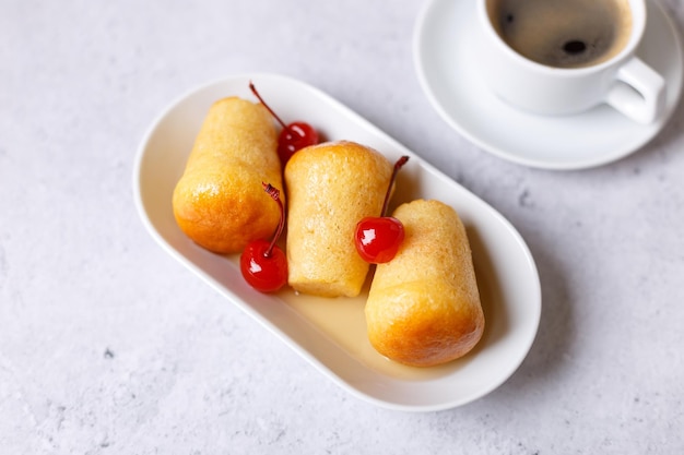 Neapolitan Rum baba or baba au rum on a white plate with a cocktail cherry and a cup of coffee