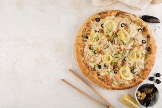 Neapolitano pizza with seafood, Caesar sauce, pink salmon, shrimp, mussels, squid, Mozzarella cheese, lemon and olives on a light background. Top view with a copy space for the text.