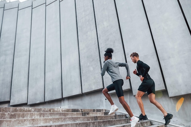 Near big wall European man and african american woman in sportive clothes have workout together