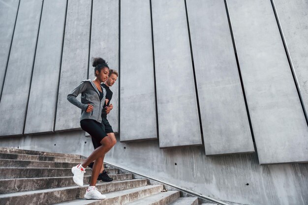 Near big wall European man and african american woman in sportive clothes have workout together