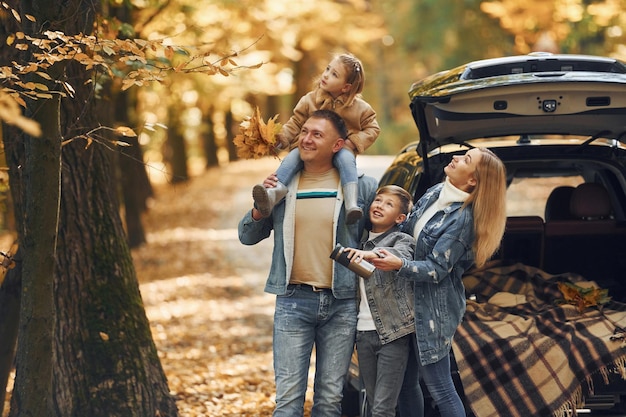 Near car with open trunk Happy family is in the park at autumn time together