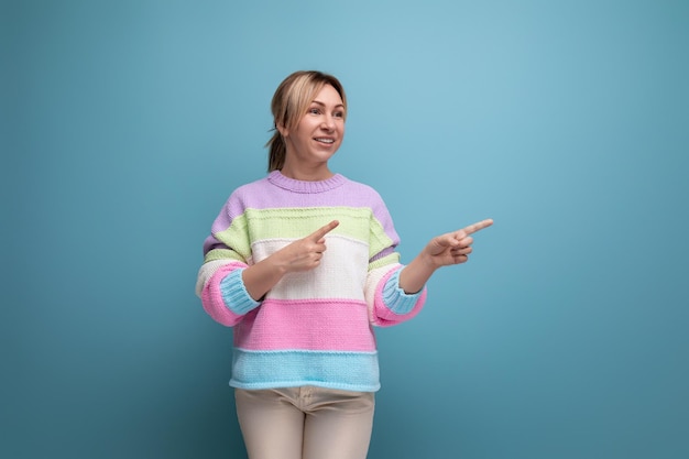 Neat cute blond woman in a casual look shows her hands at the wall with copy space on a blue