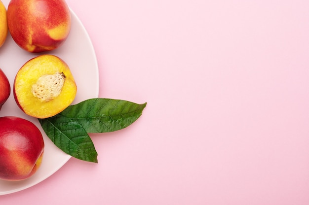 Nectarines peaches cut in slices with leaves on a pink plate on a bright background. Organic summer fruits, healthy lifestyle food, top view, copy space.