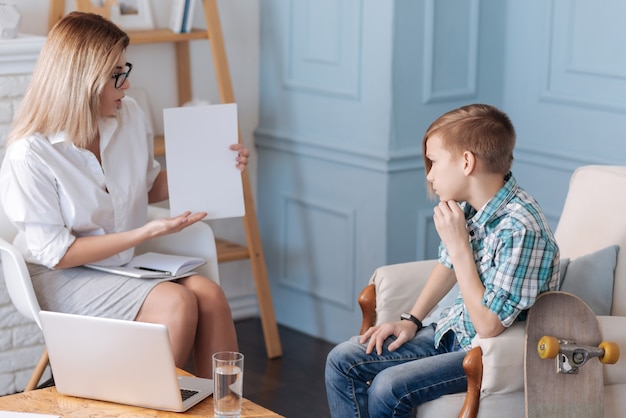 Need one second. Young teenager patient wearing casual clothes holding his left hand near chin while sitting in semi position