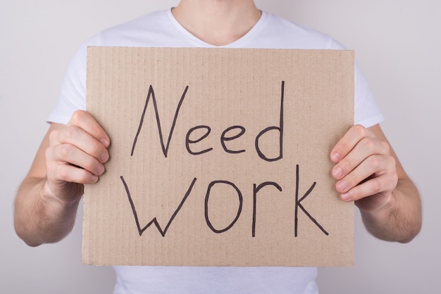 Need opened vacancy work concept. Cropped closeup photo of guy in white casual t-shirt showing carton board with text isolated over grey background