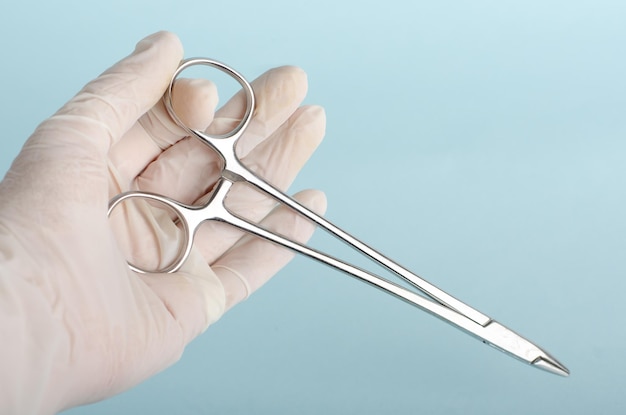 Needle holder for surgical instrumentation table on white gloves in the hands of a surgeon