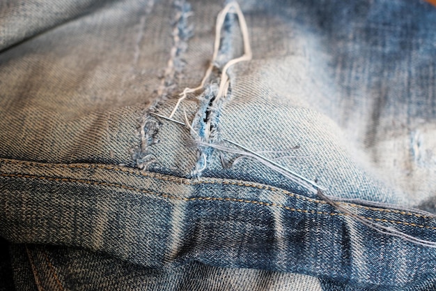 Photo a needle and thread sew up a hole in a denim work of a seamstress or tailor with a needle garment