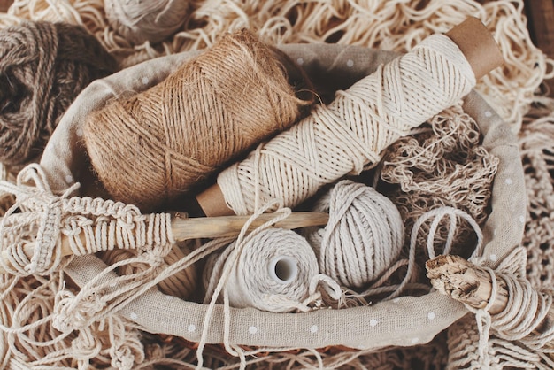 Needlework, macrame, knitting. Yarn and thread of natural colors in a wicker basket. Women's hobby.